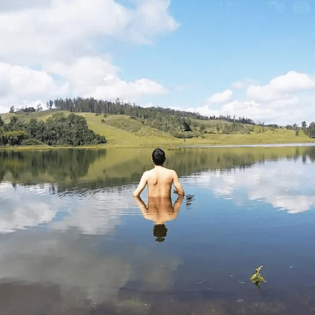 Hombre nadando en el Lago Calima durante el atardecer con montañas de fondo.